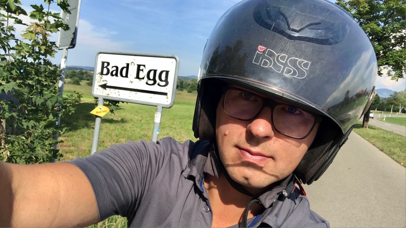 Torsten Sauter in his open-face helmet beside a road sign reading Bad Egg